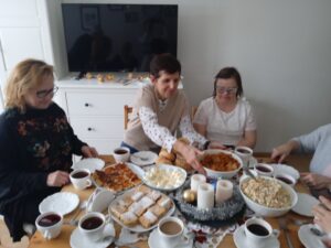uczestniczki i gości przy stole, na którym znajdują się świąteczne potrawy