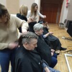Seniorki siedzą na stanowiskach fryzjerskich , maja wykonywane fryzury przez uczniów szkoły ZDZ
