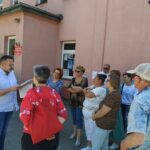 Seniorzy stoją przy MDK os. Karsznice słuchają opowieści dyrektora Zduńskowolskiego Muzeum