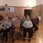Seniorzy Klubu Seniora „Lokomotywa 60 +” siedzą na krzesełkach i słuchają o twórczości Alexandra Jolliena