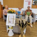 Seniorki siedzą na kanapie i czytają głośno pieśni, fraszki i treny Jana Kochanowskiego z okazji Narodowego Czytania