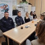 Dzielnicowi i pracownicy socjalni siedzą przy stole i omawiają sprawy