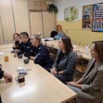 Dzielnicowi i pracownicy socjalni siedzą przy stole i omawiają sprawy