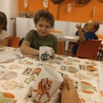 Dzieci siedzą przy stole i pokazują swoje kubki