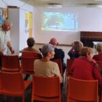 Seniorzy Klubu „Uśmiech Seniora” siedzą na krzesełkach, aby obejrzeć seans filmowy