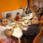 Dziewczynki siedzą przy stole, na talerzach są owoce