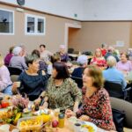 Seniorzy siedzą przy stole i konsumują przyniesione dary jesieni