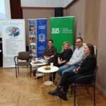 Przedstawiciele ZUS, policji, rzecznik finansowy i pracownik socjalny siedzą przy stolikach i słuchają przekazywanych informacji