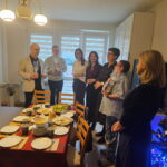 Kilka osób stoi przy stole i słucha życzeń