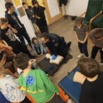Funkcjonariusz pokazuje jak wykonać resuscytacje, dzieci przyglądają się