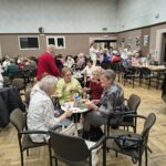 Seniorki siedzą przy stolikach podczas słodkiego poczęstunku