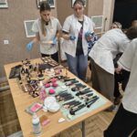 Seniorki siedzą przy stolikach i mają wykonywane zabiegi pielęgnacyjne na twarz